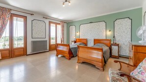 Ein Schlafzimmer mit zwei Holzbett, einem Heizkörper, einem kleinen Nachttisch, einem Sessel und einem Ventilator.