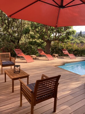 A wooden deck with lounge chairs and a table, a swimming pool, and a large tree providing shade. - VILLA en Pierre 4 persons near PORTO-VECCHIO HEATED SWIMMING POOL  (Lecci)