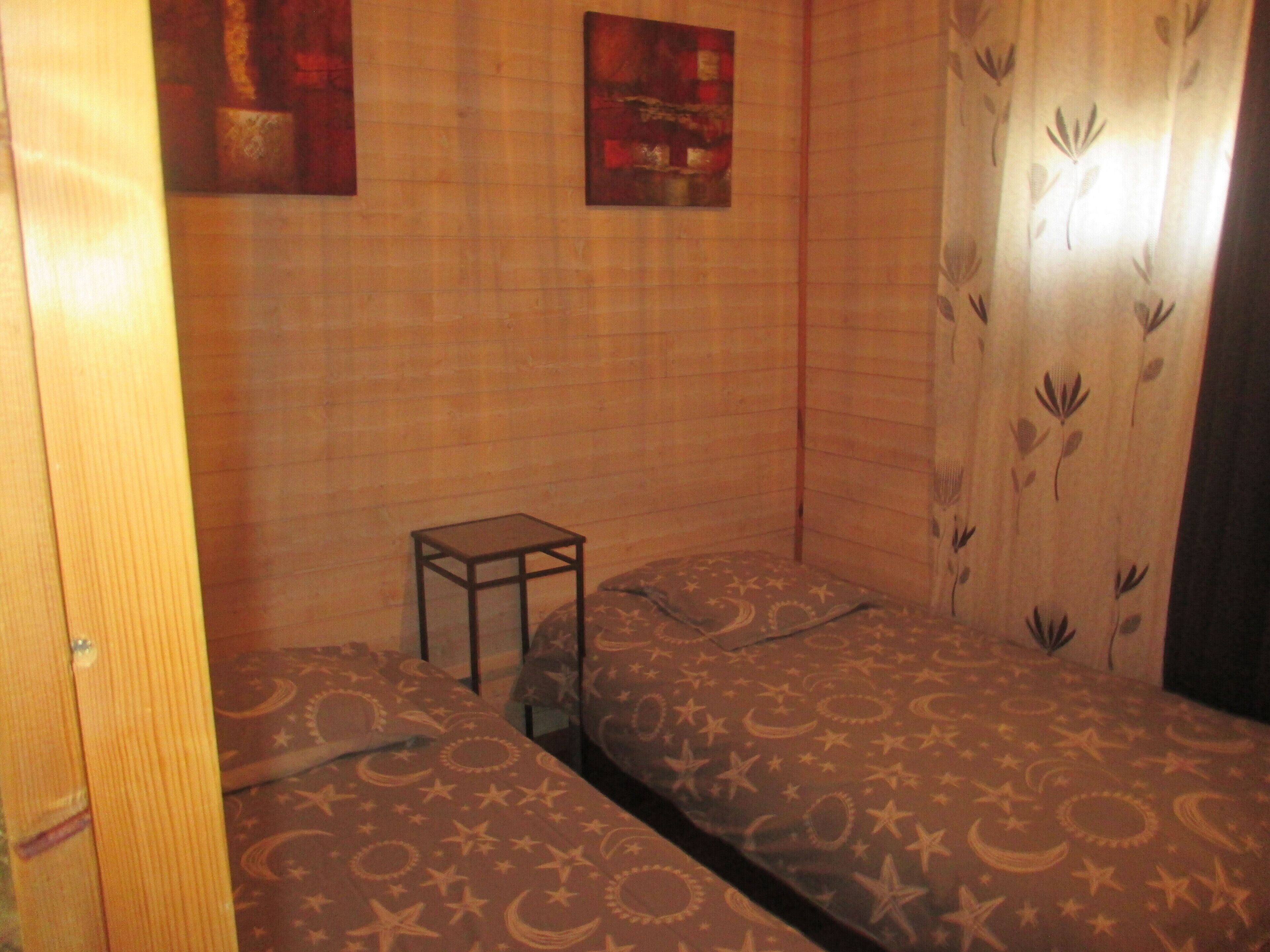 Een kamer met twee bedden, een tafeltje en een gordijn met een bladmotief.