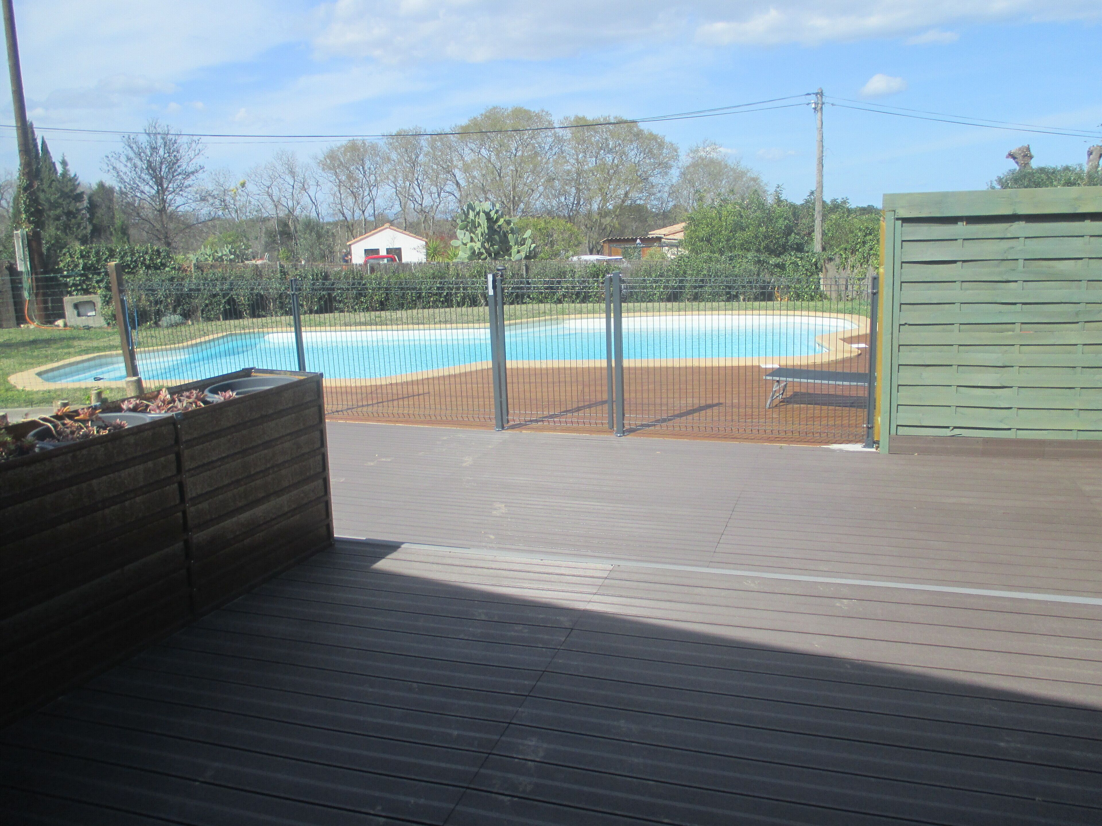 A wooden deck with a pool in the background.