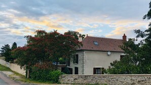 Une maison à deux étages, avec un mur en pierre à l’avant, un toit en tuiles et une antenne parabolique.
