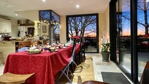 Un coin repas avec une nappe rouge, une grande fenêtre donnant sur les arbres et une plante en pot posée sur le rebord de la fenêtre.