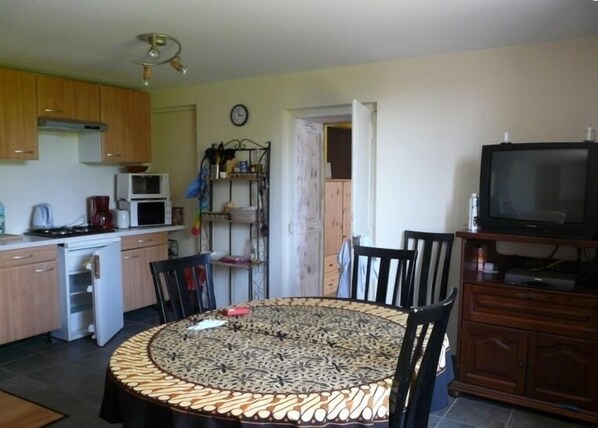 A compact kitchen with a dining area, a television, and a clock on the wall.