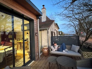 A cozy outdoor seating area with a table and chairs, a large urn, and a view of the surrounding landscape.