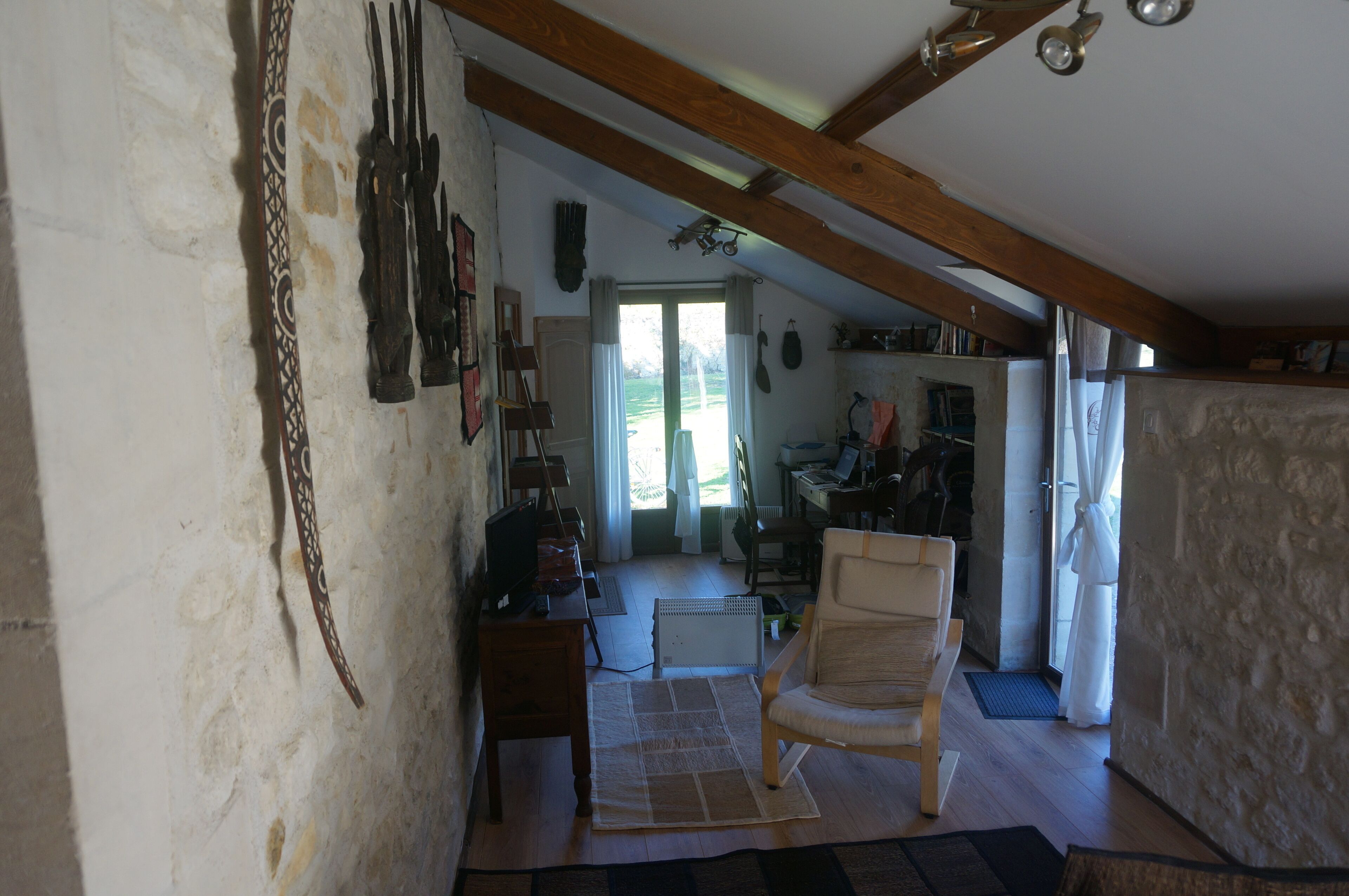 A rustic room with exposed wooden beams, a stone wall, a wooden chair, a small table, and a television.
