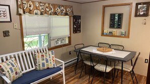 Ein gemütliches Zimmer mit einem weißen Sofa, einem Esstisch mit Stühlen, einem Fenster mit Jalousien und einem Wandspiegel.