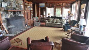 Un salon chaleureux avec une cheminée en pierre, des fauteuils en cuir, un canapé et une bibliothèque.