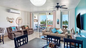 A spacious living room with a dining area, a ceiling fan, and a large TV.
