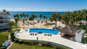 A resort with a swimming pool, beach, palm trees, and a view of the ocean.