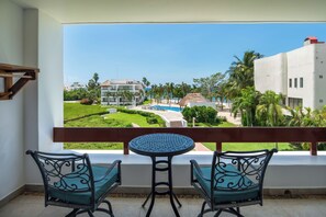 Un balcón con una mesa y dos sillas, con vistas a una piscina y edificios de un complejo turístico.