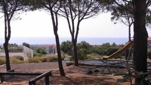A playground with a slide and swings, surrounded by trees and a view of the sea.
