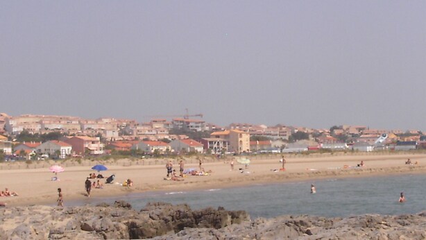 A beach with people, umbrellas, and buildings in the background.