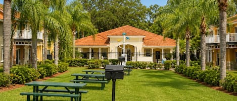 Un patio con un edificio de techo rojo, rodeado de palmeras y césped verde.