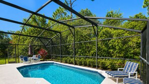 A swimming pool with a glass enclosure, surrounded by lounge chairs and a covered patio area. - LAKE BERKLEY-(1059LB) - 4BR 3BA Pool Home, 2 Master Suites, gated Resort (Kissimmee)