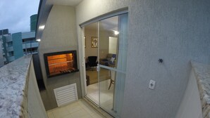 Un balcón con una parrilla incorporada, una puerta corrediza de vidrio que da a un espacio de estar y vistas de la ciudad.