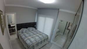 Un dormitorio con cama, mesita de noche, espejo y baño visible a través de una puerta abierta.