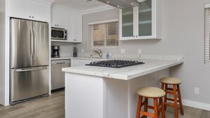 Een moderne keuken met witte kasten, een roestvrijstalen koelkast, een magnetron, een gasfornuis en een raam met zonwering.