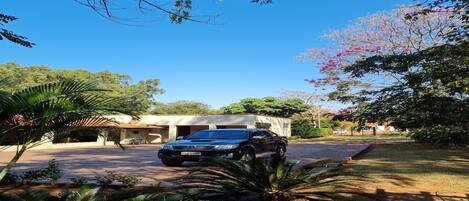 Un SUV negro estacionado frente a un edificio con garaje, rodeado de plantas y árboles tropicales.
