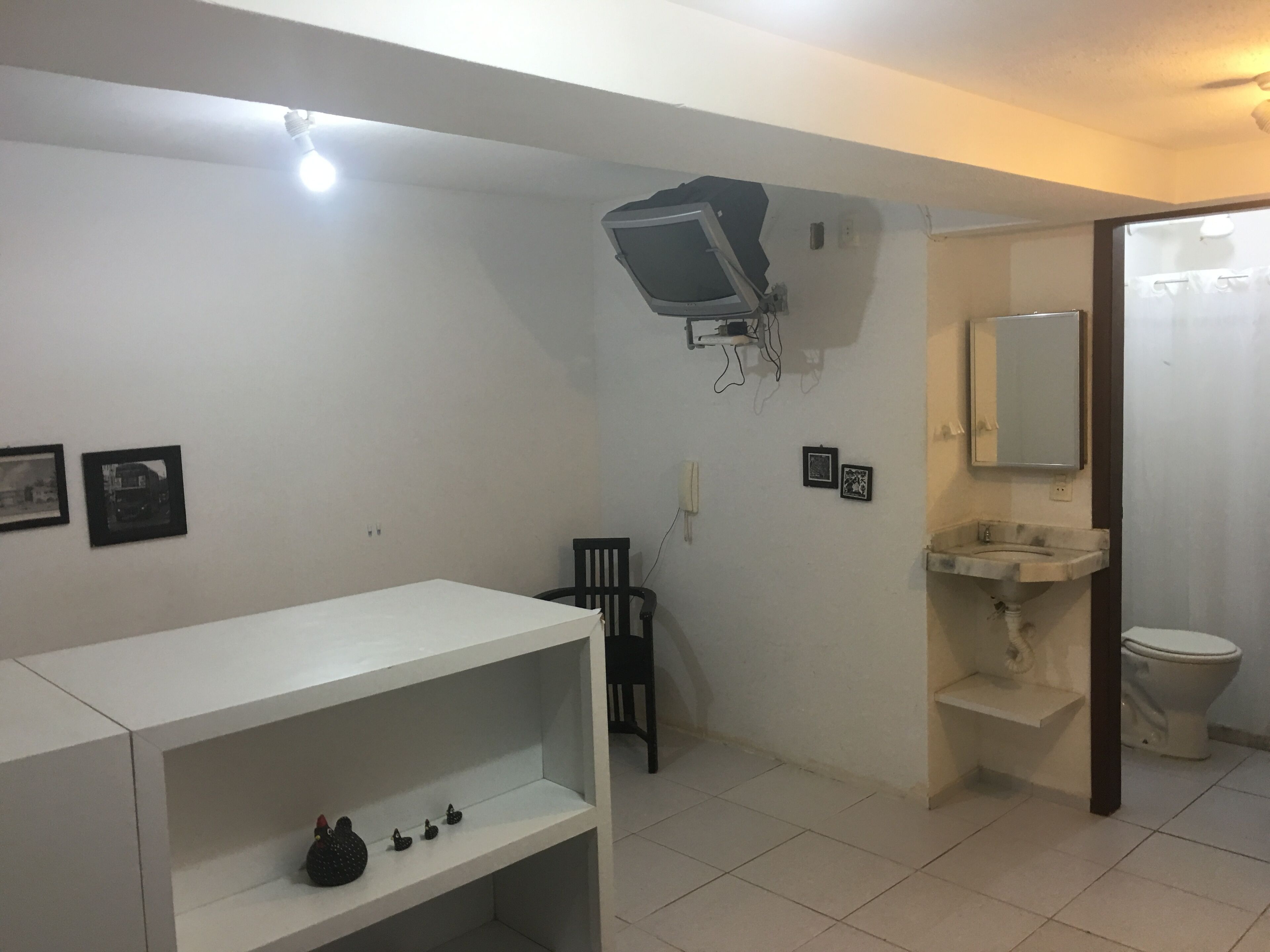 A bathroom with a white sink, toilet, and a shelf with decorative items. There are two framed pictures on the wall.