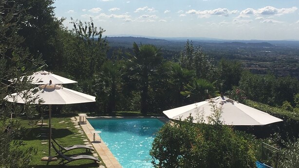 A backyard with a swimming pool, surrounded by greenery and two umbrellas. - chaming little house with pool facing the most  beautiful tuscan scenary  (Lucca)