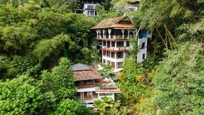 Un edificio de varios pisos con balcones, rodeado de abundante vegetación.