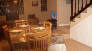 Comedor con una mesa dispuesta para cuatro personas, sillas de madera y un televisor sobre un mueble.
