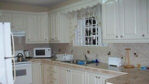 Una cocina con armarios blancos, un microondas, un hervidor y un lavabo.