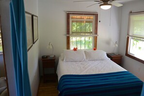 A bedroom with a bed, a nightstand, a desk, a ceiling fan, and a window with blinds.