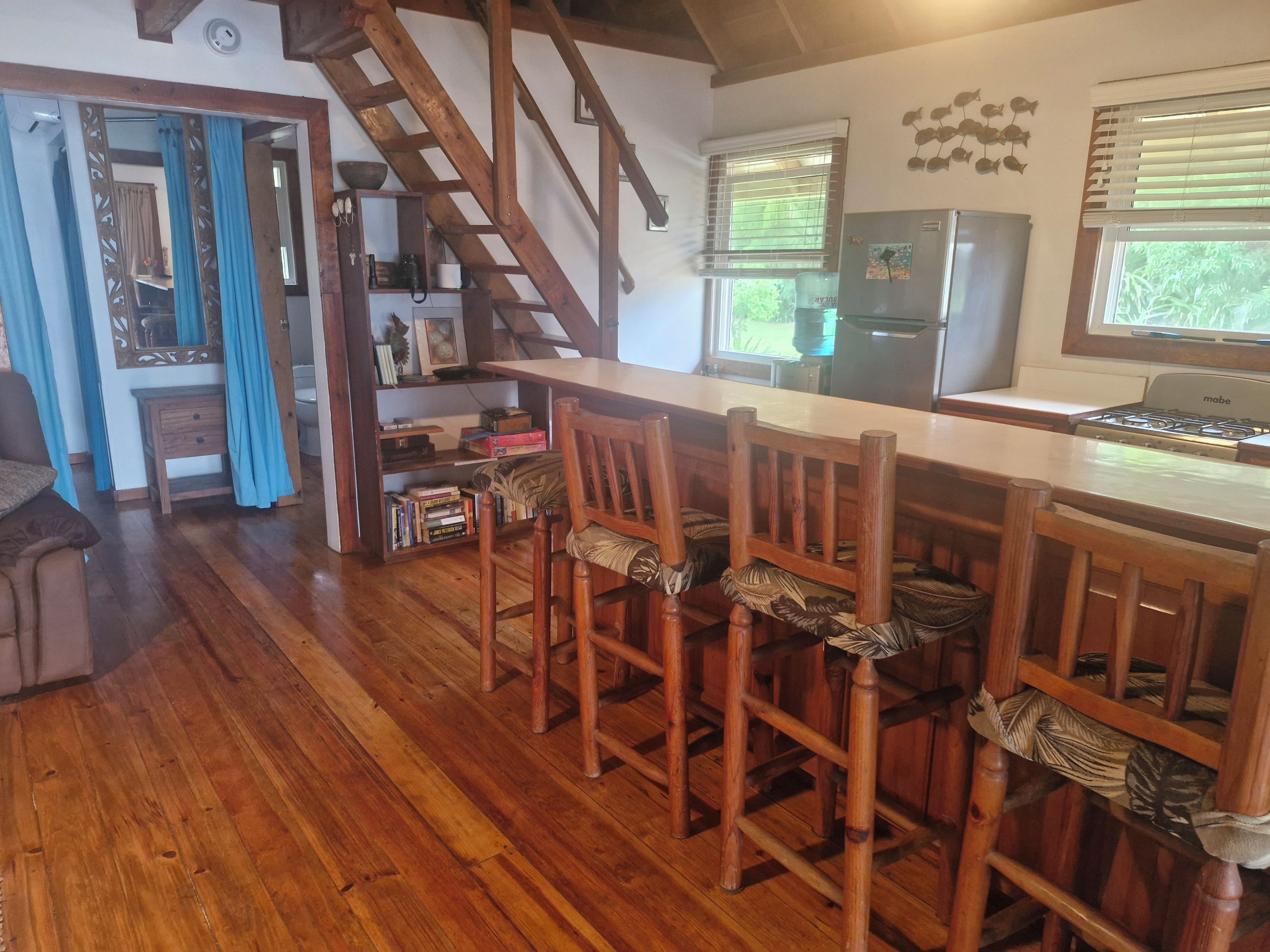 A kitchen with wooden chairs, a wooden table, a refrigerator, and a window with blinds.