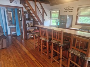 Una cucina con sedie e tavolo in legno, un frigorifero e una finestra con persiane.