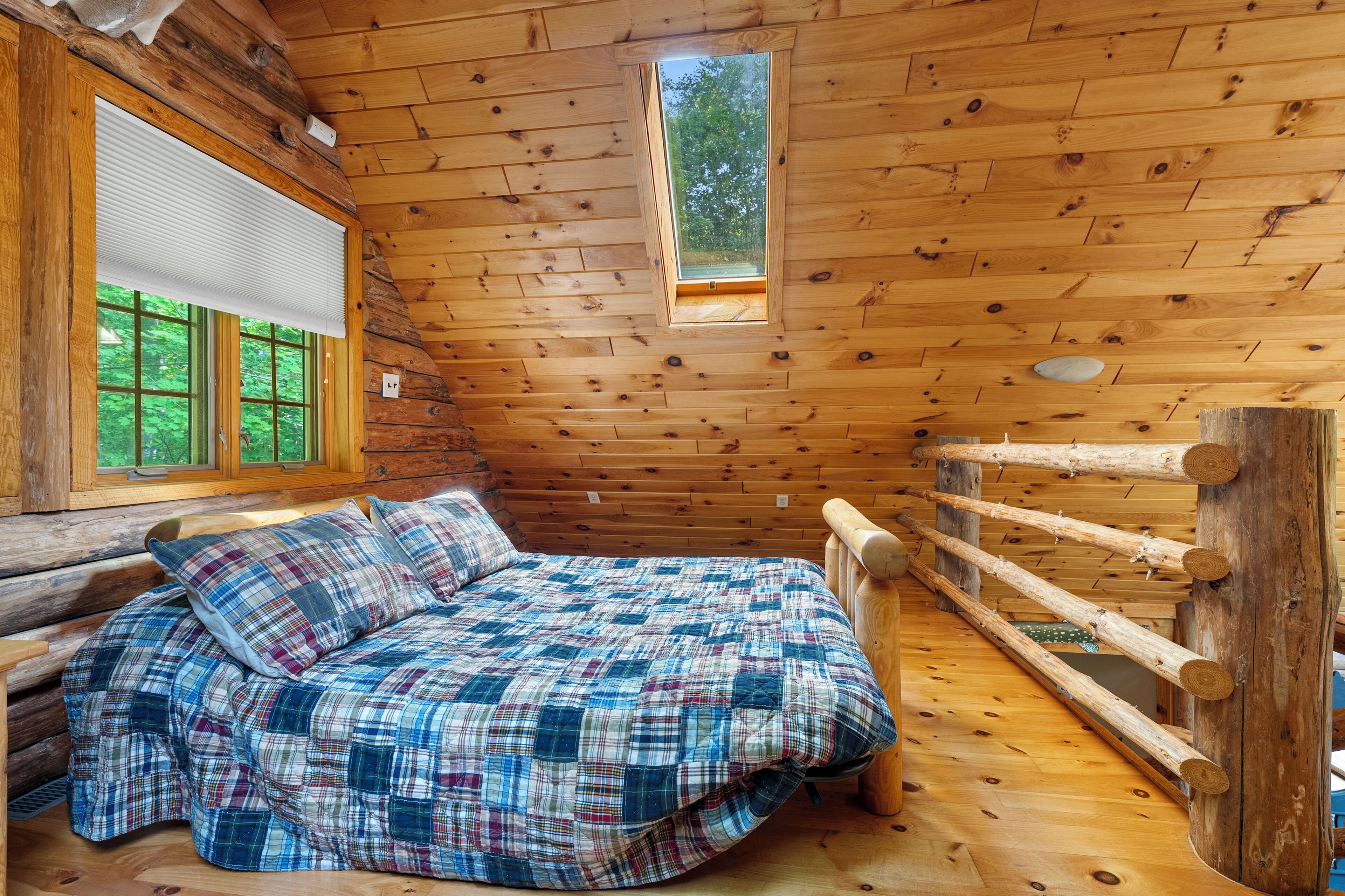 Ein Schlafzimmer in einer Blockhütte mit einem Bett, einem Fenster und einer Holzkονstruktion an der Decke.