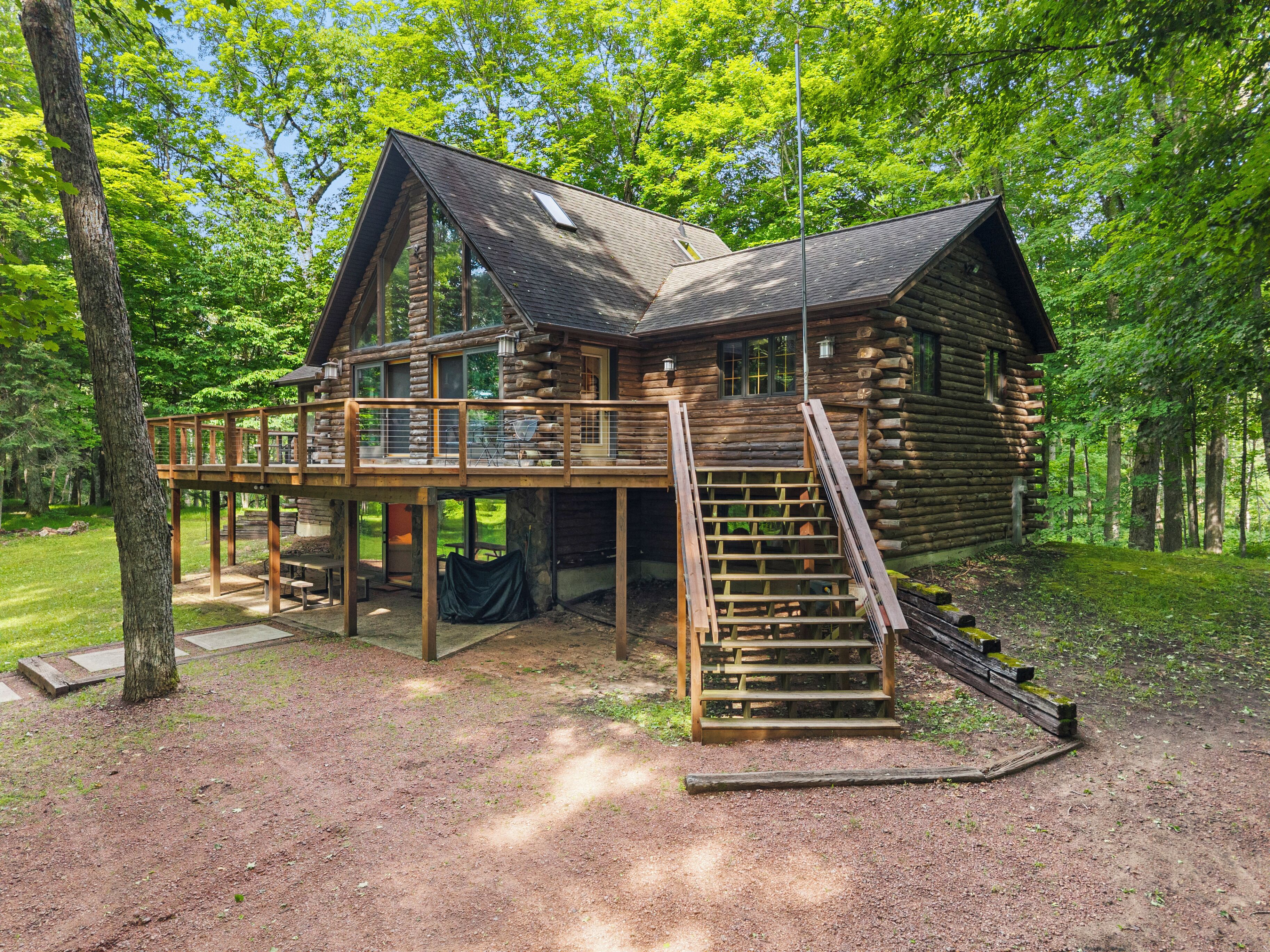 A log cabin with a deck, a staircase, and a covered outdoor seating area.