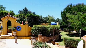 A courtyard with a yellow building, a stone wall, and a blue umbrella. - Half hectare property, 6 comfort rooms w/private AC&Bathroom, garden, pool, 4-12 persons (Alvor)