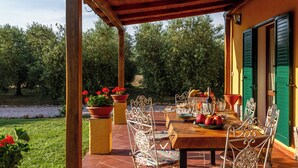 Eine Terrassengruppe mit Holztisch, gedeckt für ein Essen, umgeben von Metallstühlen mit gemusterten Kissen.