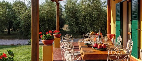 Un patio al aire libre con una mesa de madera lista para comer, rodeada de sillas de metal con cojines estampados.
