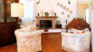Ein Wohnzimmer mit Kamin, zwei Sesseln, einem Fernseher und einer Lampe.