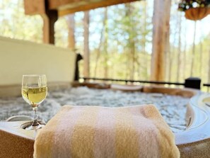 Wellness omgeving met een glas witte wijn op een handdoek, een jacuzzi en uitzicht op bomen.