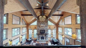 Un chalet spacieux doté d’une cheminée en pierre, de nombreuses fenêtres et d’un grand ventilateur de plafond.