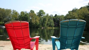 Dos sillas Adirondack frente a un lago con una orilla boscosa.