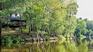 Una cabaña junto al lago con una terraza, rodeada de árboles y un cuerpo de agua tranquilo.