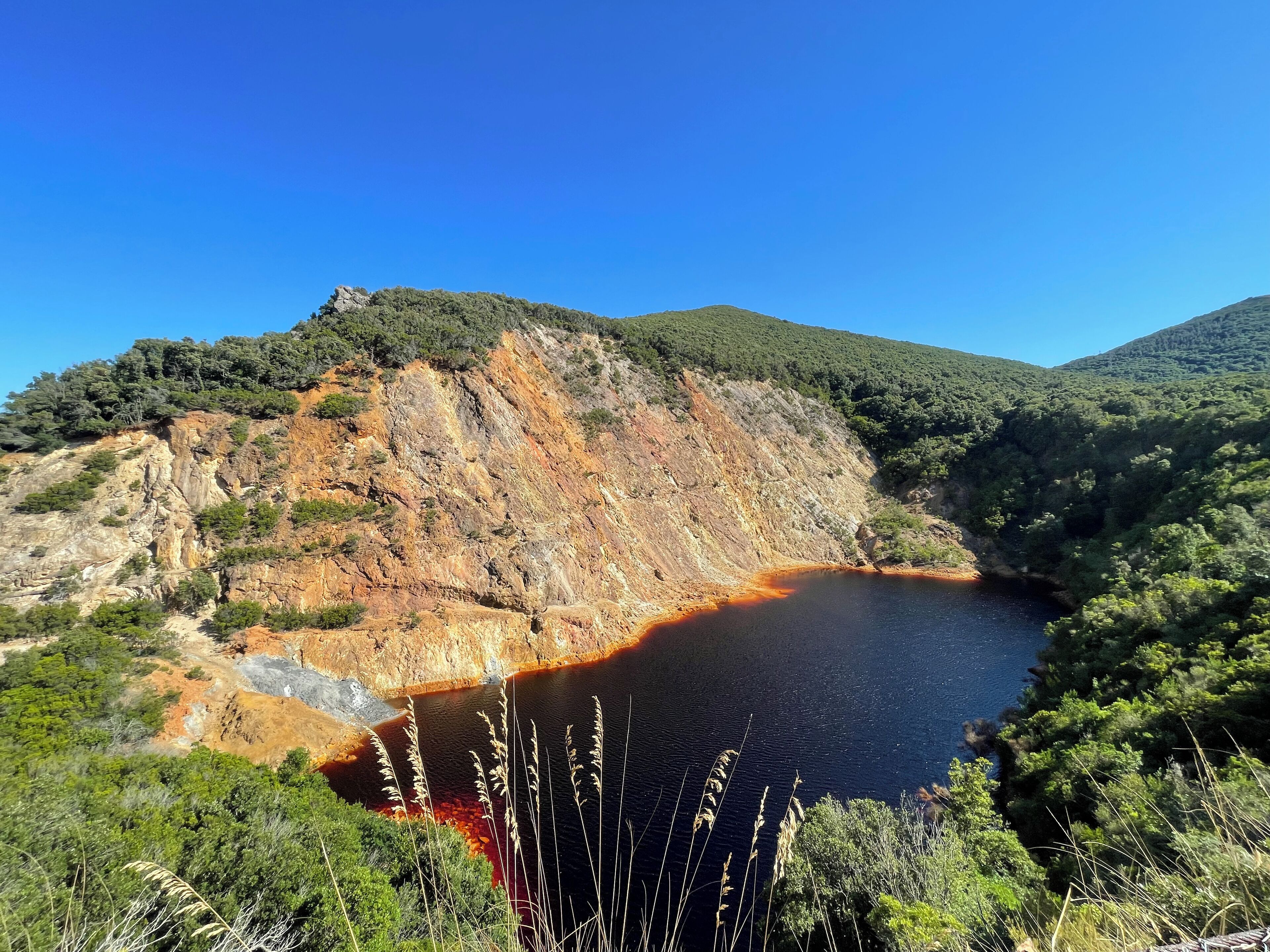 A natural landscape with a lake surrounded by rocky cliffs and dense greenery.