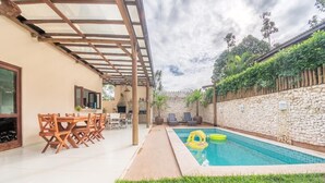 Un'area esterna coperta con piscina, arredi in legno e pareti in pietra.