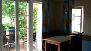 Une pièce comprenant une table à manger en bois, des chaises et une porte-fenêtre coulissante donnant sur un espace extérieur verdoyant.
