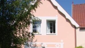 Une maison à deux étages avec un toit en pente, un porche à l’avant avec une table et des chaises, et un petit jardin.