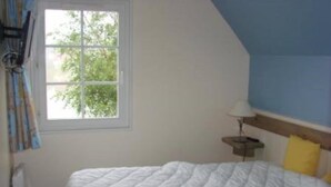 Une chambre à coucher avec un lit, une fenêtre, une lampe et un mur agrémenté d’une touche de bleu.