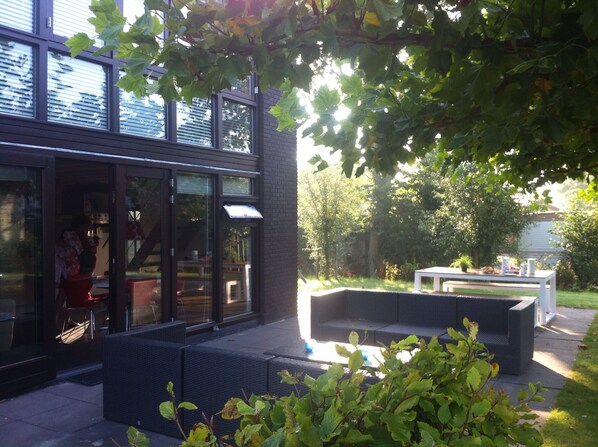 An outdoor seating area with a modern design, a glass entrance, and a view of the surrounding greenery.