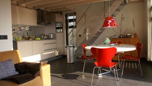 Eine moderne Küche mit Essbereich, inklusive Treppe, einem Esstisch mit roten Stühlen und einer Couch mit einem gemusterten Kissen.