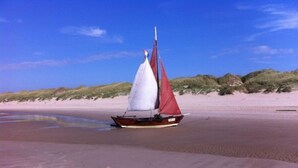 Ein Segelboot an einem sandigen Strand mit Dünen im Hintergrund.