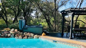 A clear swimming pool with a stone wall and a hot tub in a shaded area with trees.