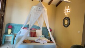Un dormitorio con cama con dosel, ventilador de techo, lámpara de pared decorativa y una silla de mimbre.